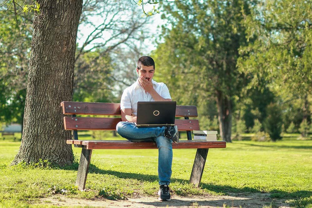Man sitting on a park bench reading a loan agreement from his computer to spot hidden fees.