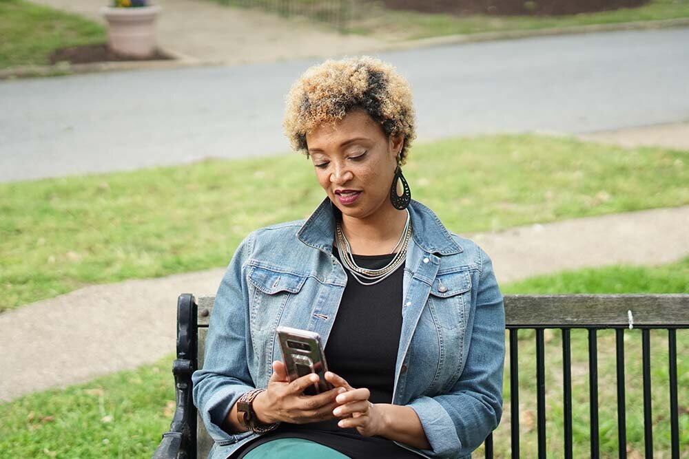 A black woman sitting on a bench at a park using a smartphone