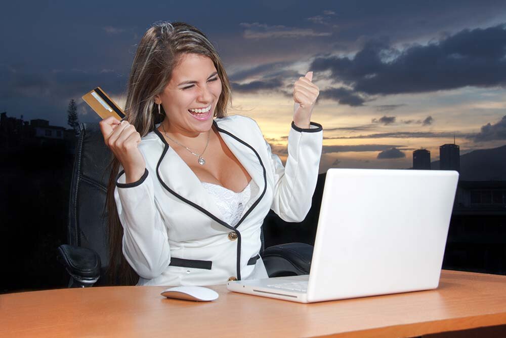 An excited woman in a white suit sitting at a desk using a laptop computer 