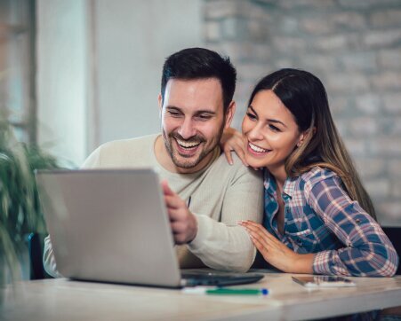 Happy couple sitting at a table looking over a laptop