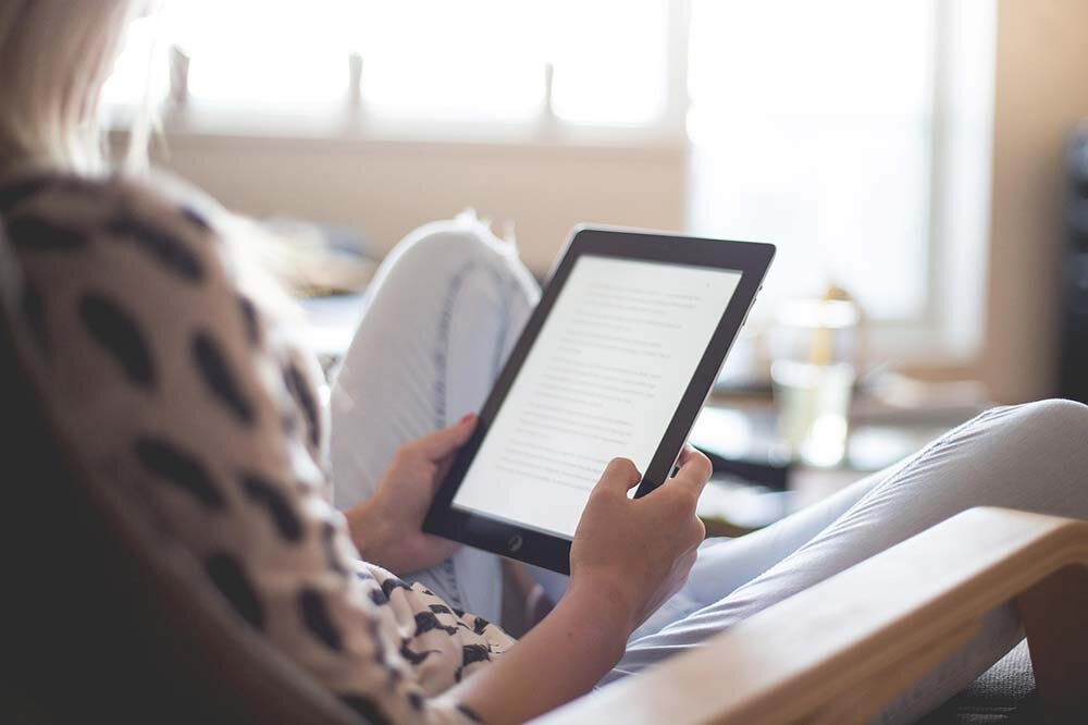 Woman seated on a couch reading loan agreement on a tablet.