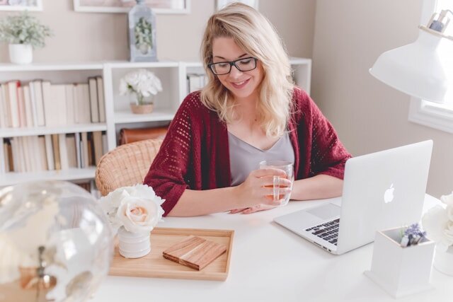 Woman seated at a desk with a laptop holding a glass mug.