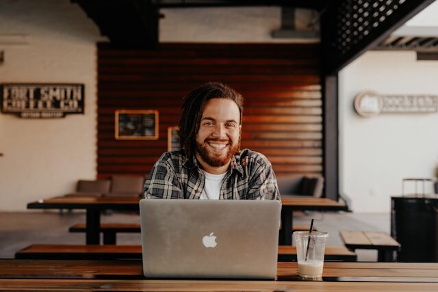 Man in pleated shirt sitting at a table in front of a laptop