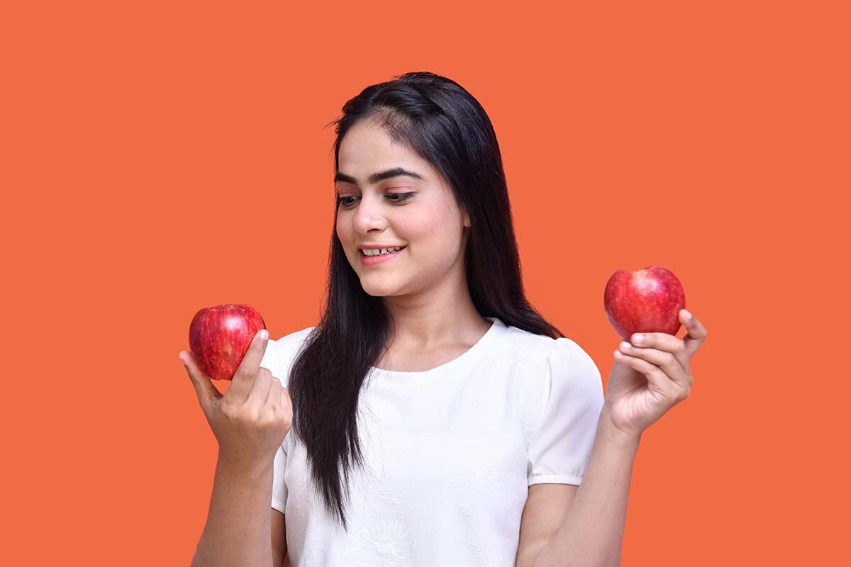 A young woman holding up apples in each hand and looking at one