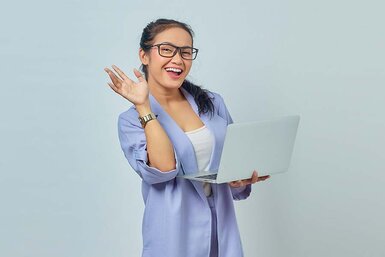 A happy woman standing wearing glasses holding a laptop