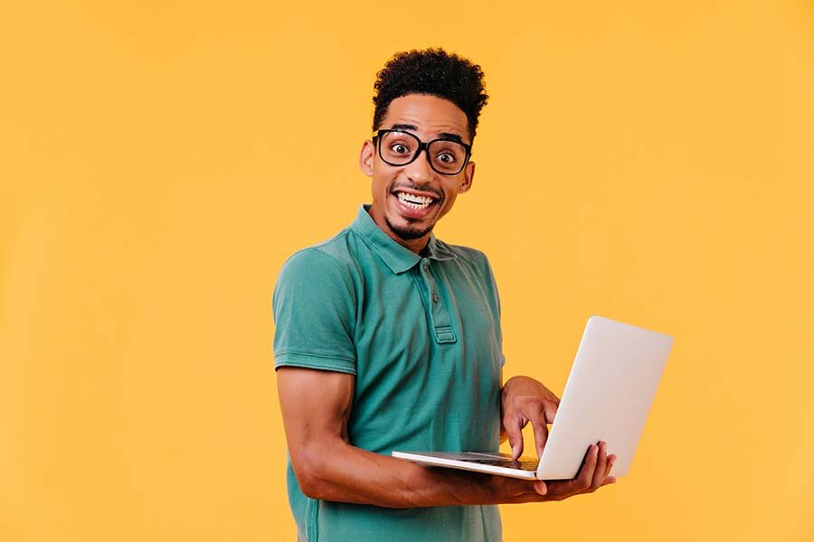 A happy man in a green shirt and glasses standing holding a laptop computer