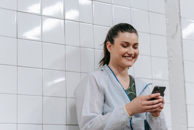 Smiling female healthcare worker receiving notification of installment loan approval on her phone