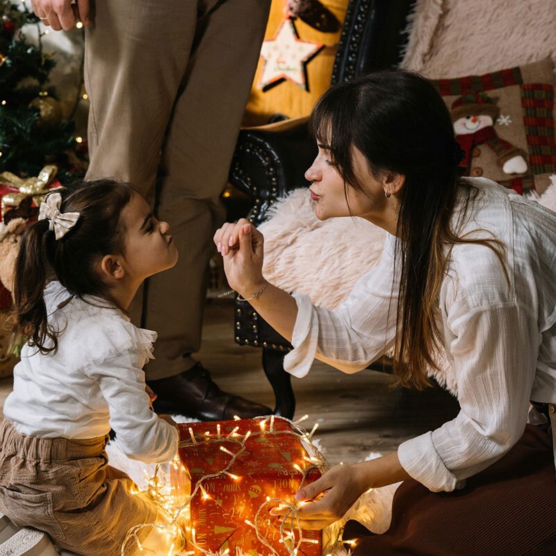 A mother and her daughter sitting on the floor to open Christmas presents.
