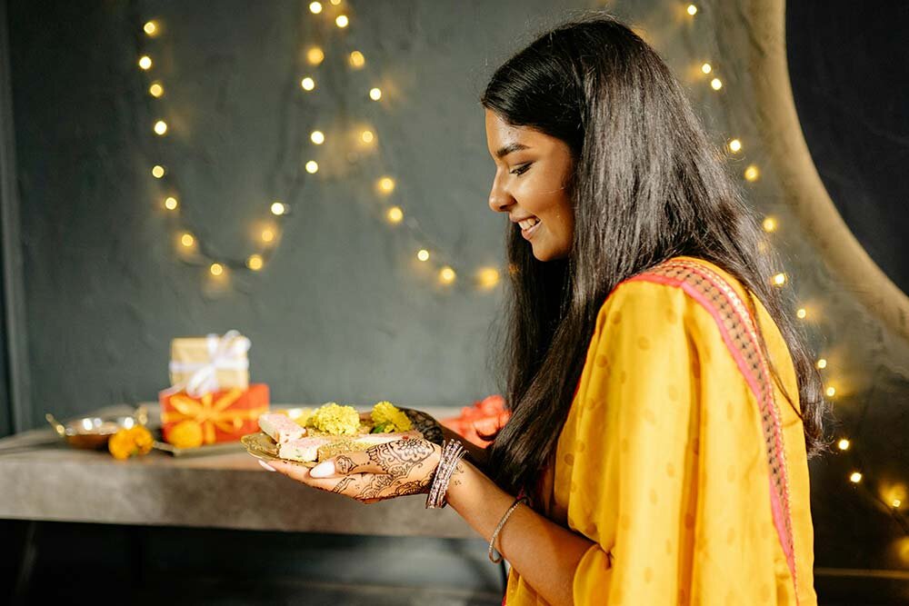 Woman celebrating Diwali with food and gifts.