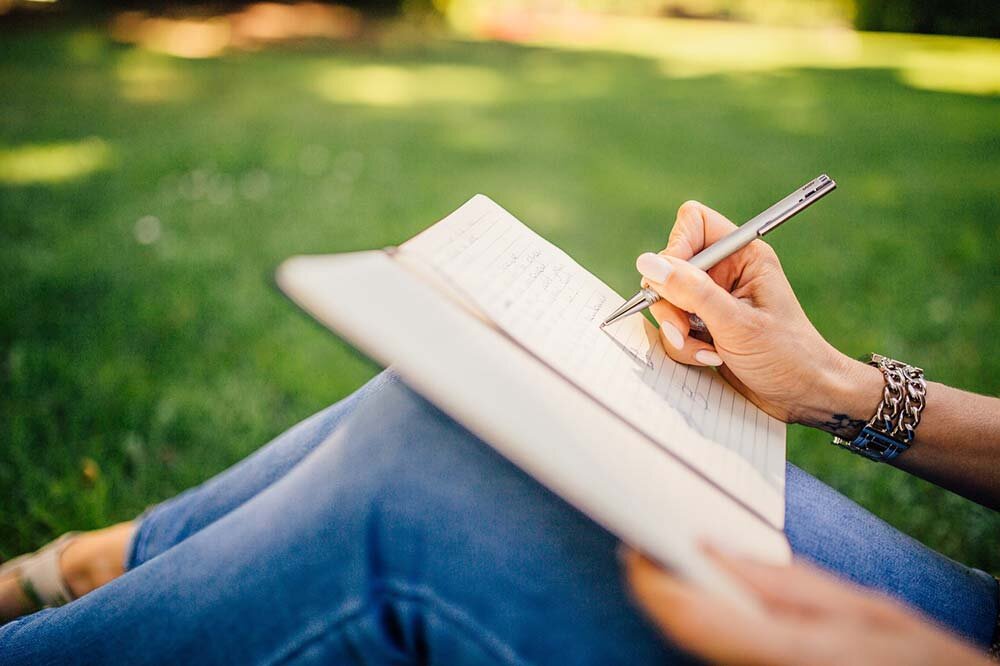 A woman seated in a grass field journaling