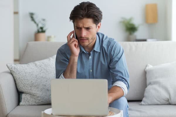 A worried young man using his laptop while on a phone