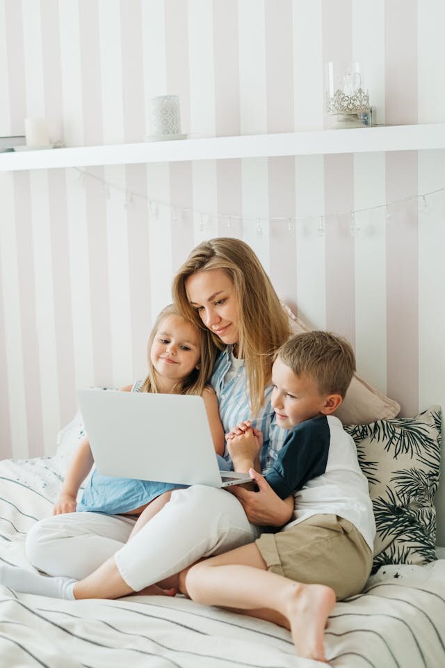 Mother sitting on bed with children looking at laptop computer.