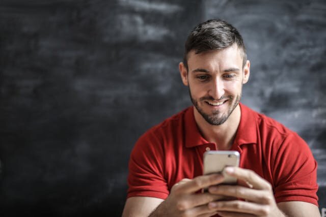 Smiling man with red polo shirt using a smartphone to apply for a personal loan in Alabama.