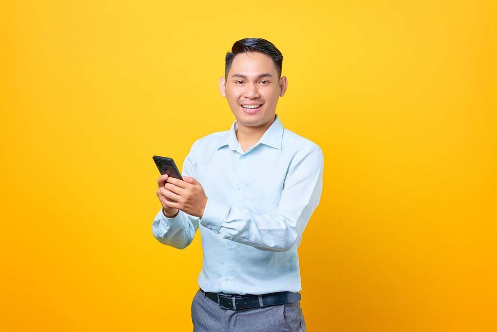 Happy young businessman holding out his smartphone with both hands