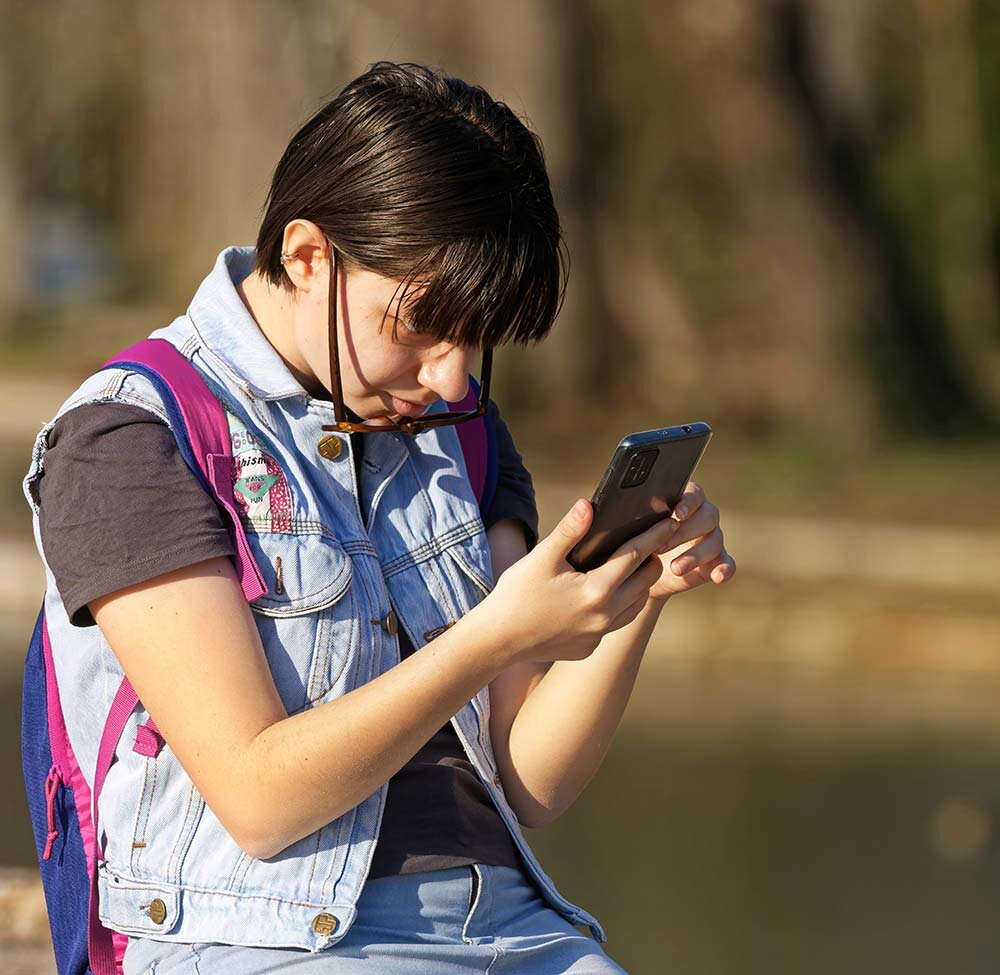 A young woman carrying a backpack and using a smartphone