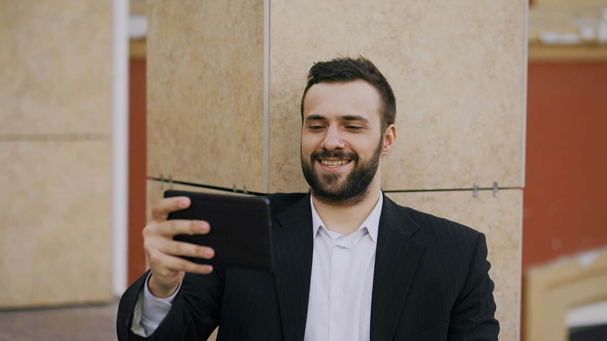 A man in a black suit and white shirt looking at a tablet, happy to qualify for an installment loan.