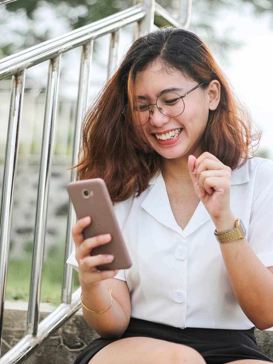 A happy woman in a white shirt seated using a cell phone