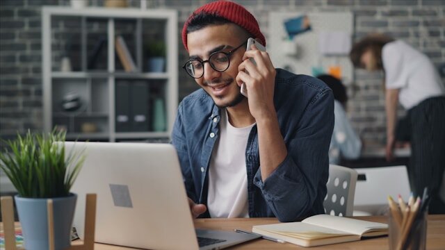 Man sitting at a desk talking on a cellphone.