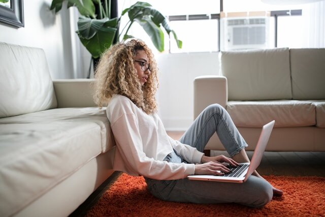 Woman sitting on the floor leaning on a couch using a laptop