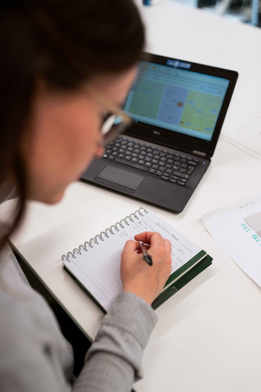 Woman studying from a laptop and writing down in a notebook