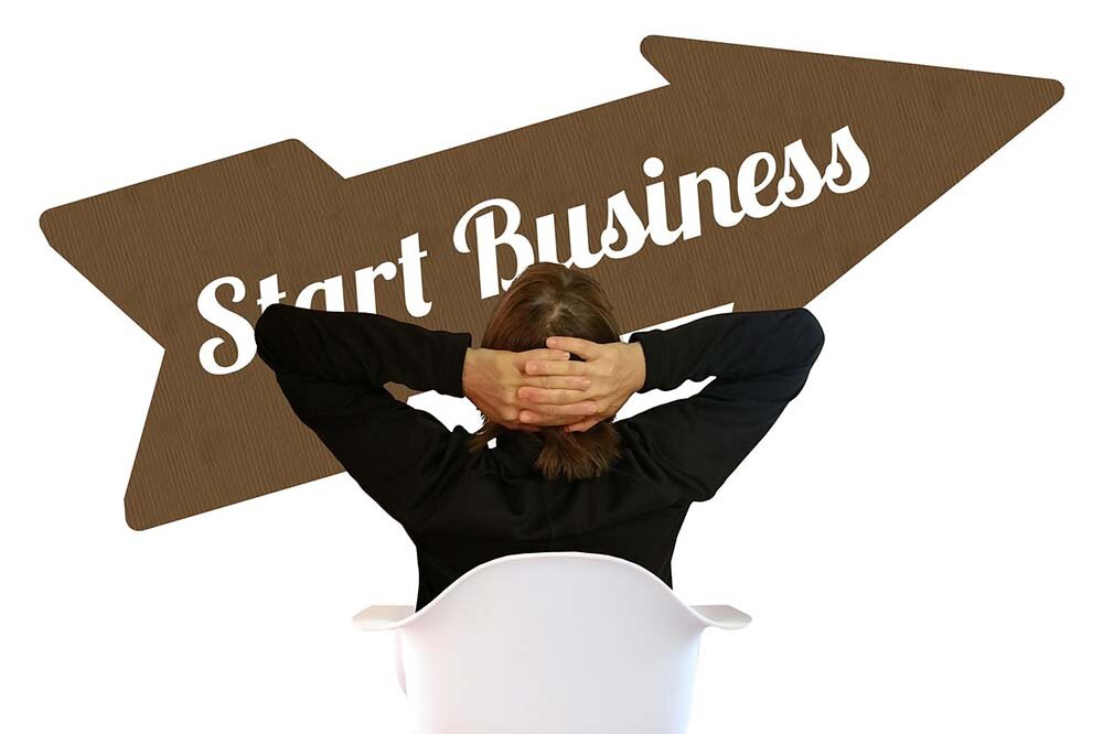 A man sitting on a chair, fingers crossed behind his head looking at an arrow pointing up written ‘Start Business’