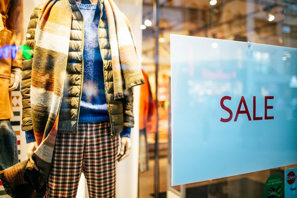 A mannequin in a window display with a sale sign