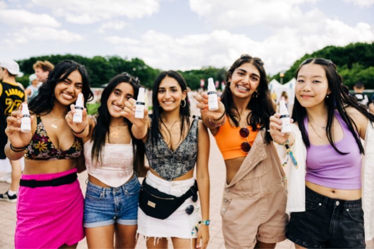 Group of girls at Lollapalooza Music Festival holding up Actiiv SPF 30 Hair + Scalp Defense sunscreen spray