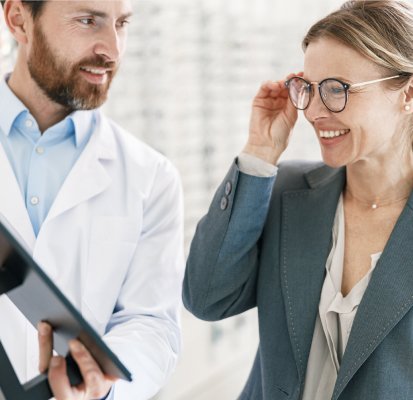 Optician holding a mirror to show patient how they look in a pair of glasses they are trying on after an eye exam