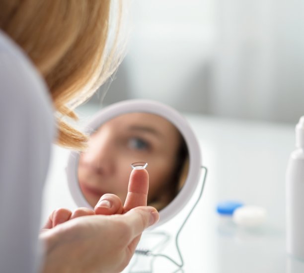 Young woman sitting in front of a small mirror to insert a contact lens