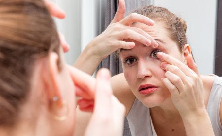 Woman using a mirror to insert a contact lens