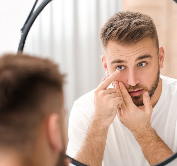 Young man using a mirror to insert a contact lens