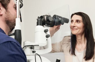 A person undergoes an eye examination using a slit lamp while an optometrist adjusts the equipment.