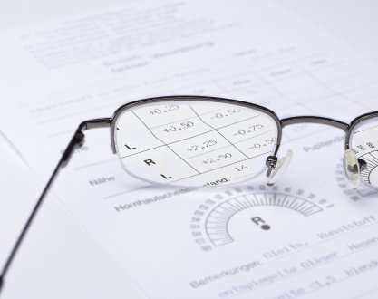 Glasses on top of a paper with a contact lens prescription in focus through the lens
