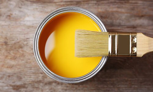 A can with yellow paint and a brush on a wooden background, top view.