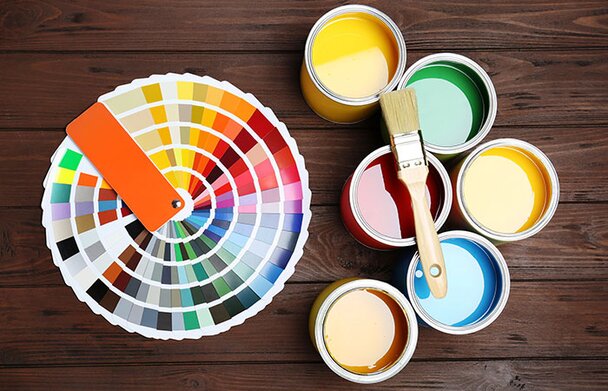 Rainbox of paint swatches, 6 bright cans of paint and a clean brush laying on top.