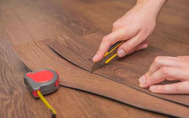 Hands using a box cutter to cut vinyl plants on the floor.