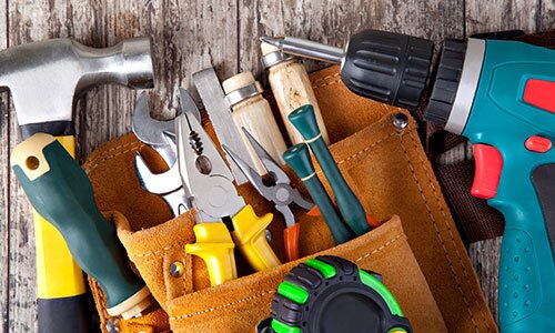 A mix of power tools and hand tools in and around a tool belt.