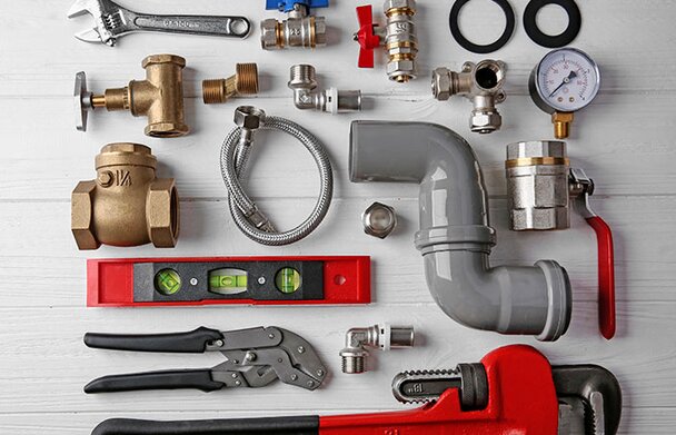 Plumbing tools and supplies neatly laid out on white wood background.