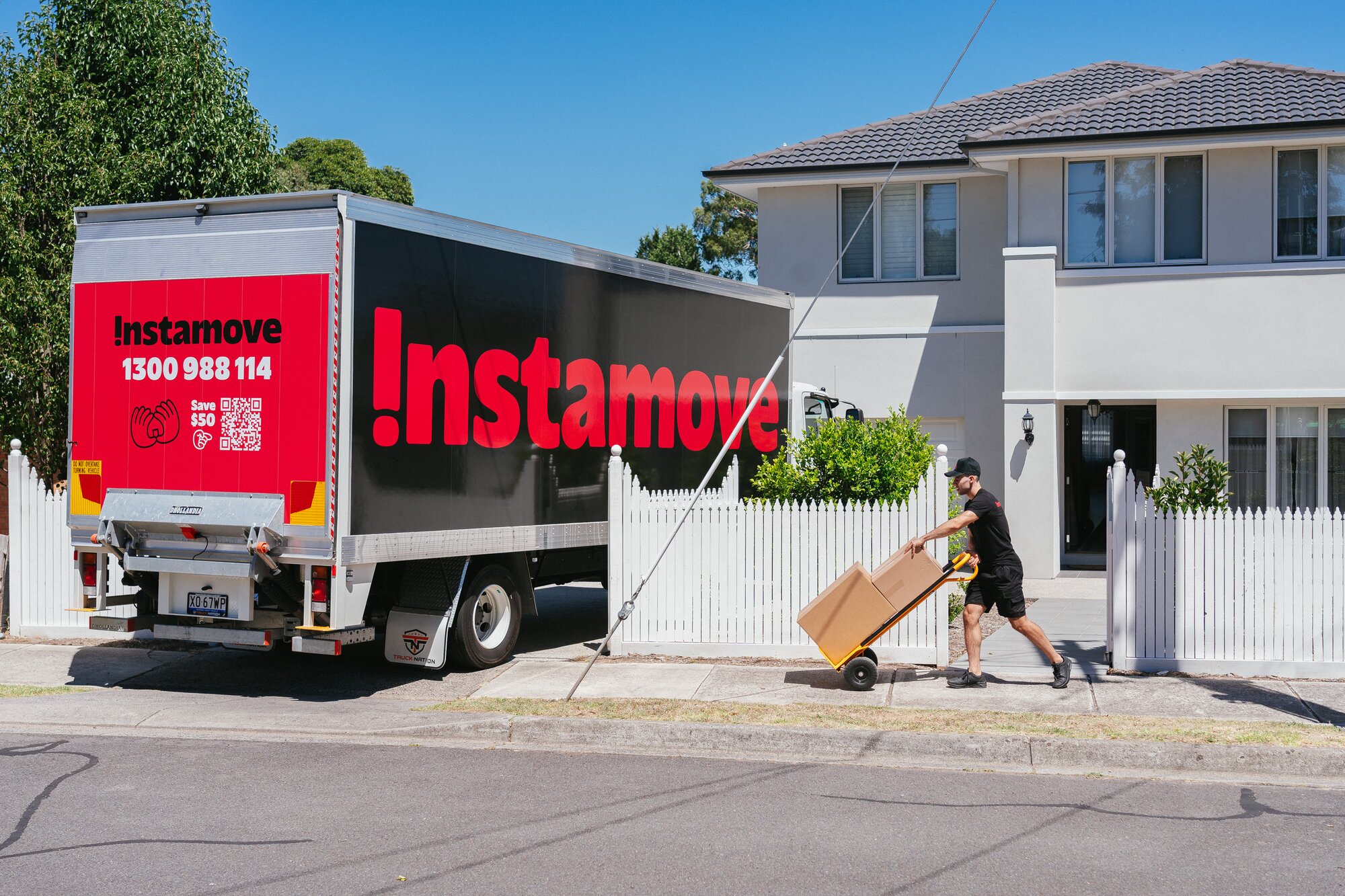 Removalist moving labelled boxes on a hand trolley into an Instamove truck