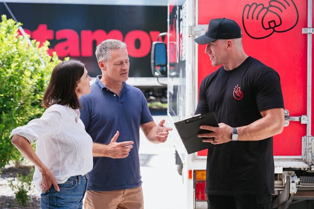 Instamove mover reviewing a clipboard of items with a couple beside a branded moving truck during morning briefing