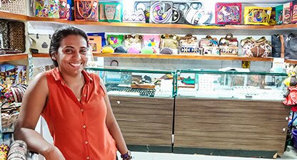 Shop owner standing next to wall of handbags