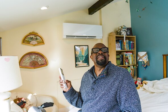 Will Hammond Jr holding a remote showcasing the controls for his space heating unit in his room.