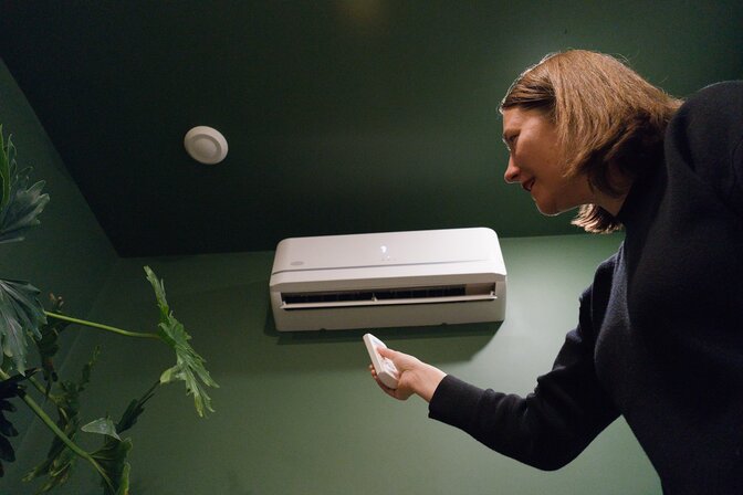 woman holding remote in front of ductless mini-split wall unit