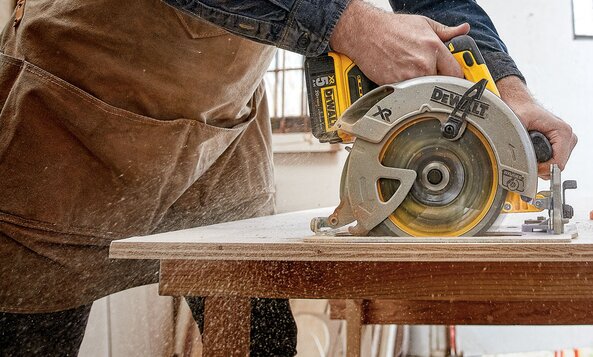 A DeWalt cordless circular saw cutting a sheet of wood.