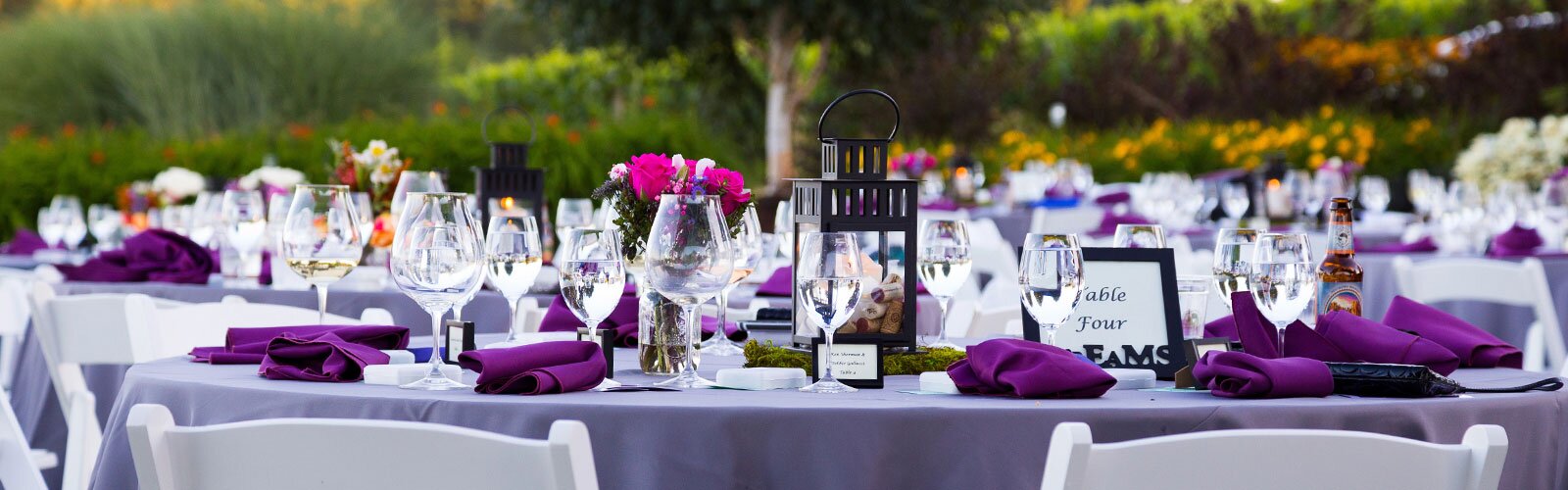 A lovely round table set for an outdoor event, with purple features and a lantern as the centerpiece. 