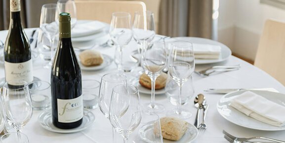 A round table set for a wedding: wine bottle, wine glasses, place settings