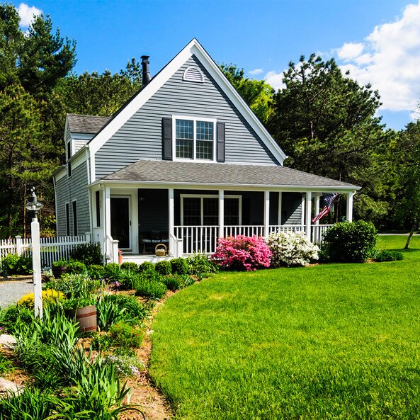 A home exterior with a wide, green lawn on a sunny day. The USA flag hung from the porch. 