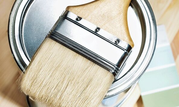 A paint brunch sits on top of paint can, colour pallet out of focus in the background.