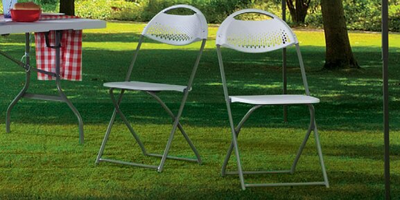 Two white folding chairs are outside in a park.