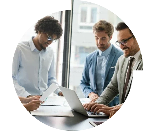 Three men at a standing desk working on a laptop.